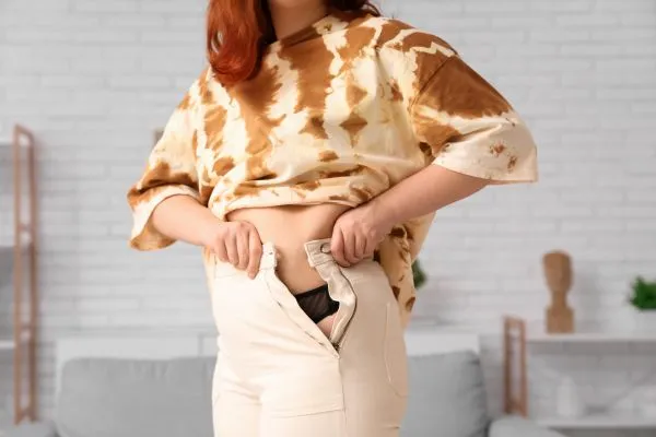 Image of woman trying to do her trousers up after pregnancy weight gain Westminster
