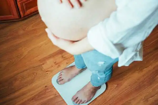 Image of woman weighing herself and experiencing weight gain through pregnancy Westminster